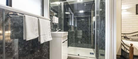 A modern bathroom with a glass-enclosed shower, a white sink, and a wooden floor.