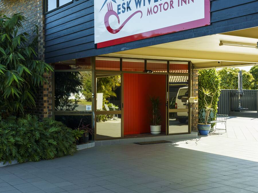 The exterior of Esk Wivenhoe Motor Inn with a clear entrance, potted plants, and a visible vehicle in the background.