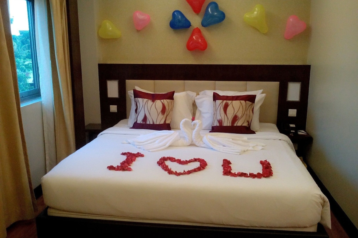 Una habitación de hotel con una cama bien hecha, almohadas y una decoración con forma de corazón en la pared.