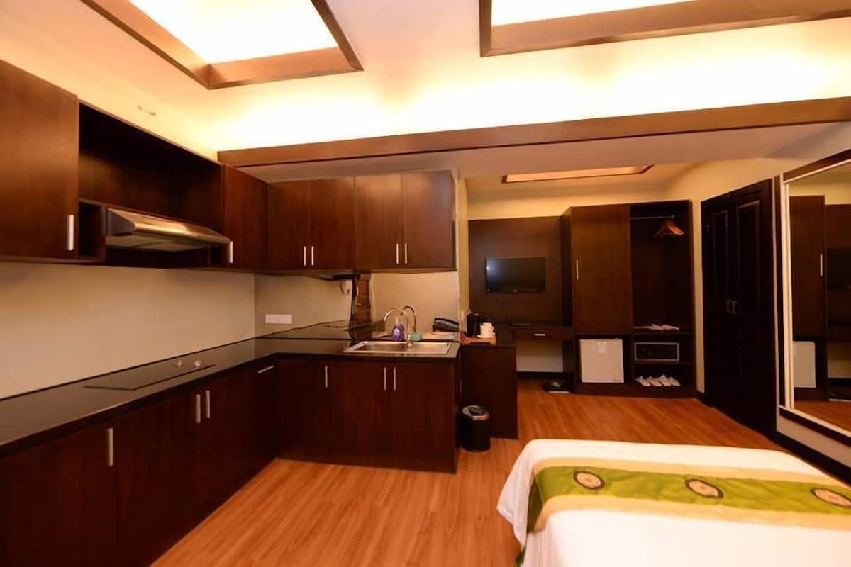 Habitación de hotel compacta con kitchenette, cama, espejo y armario.