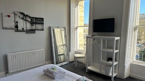 Hotellihuone, jossa on sänky, televisio, patteri, ikkuna, josta on näkymä, ja taideteoksia seinällä.