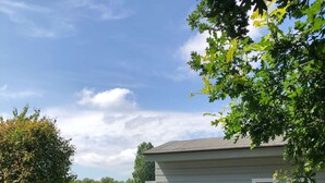 A house with a dock extending into a calm body of water, surrounded by lush greenery and vibrant purple hydrangea bushes. - Charming reed roof Lakehouse, with surrounded garden, trampoline and watersports option (Haren)