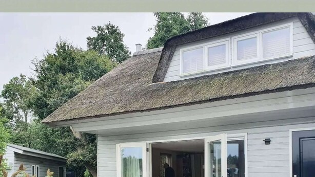 A modern house with a patio area featuring a sofa and a chair, a small table, and a bookshelf. - Charming reed roof Lakehouse, with surrounded garden, trampoline and watersports option (Haren)