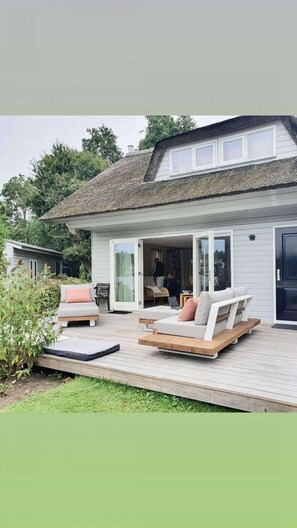 A modern house with a patio area featuring a sofa and a chair, a small table, and a bookshelf. - Charming reed roof Lakehouse, with surrounded garden, trampoline and watersports option (Haren)