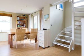 A modern living room with a dining area, a bookshelf, a white cabinet, and a staircase. - Charming reed roof Lakehouse, petfriendly with surrounded garden and trampoline. (Haren)