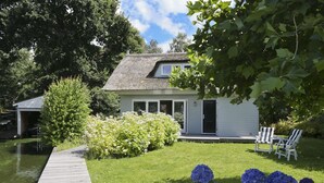 A house with a thatched roof, a small porch, and a garden with hydrangeas. - Charming reed roof Lakehouse, with surrounded garden, trampoline and watersports option (Haren)