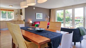 A dining area with a wooden table, wicker chairs, and pendant lights. - Charming reed roof Lakehouse, with surrounded garden, trampoline and watersports option (Haren)