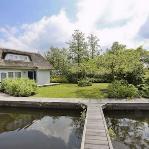 A house with a thatched roof, a grassy yard, and a wooden dock extending into a calm body of water. - Charming reed roof Lakehouse, petfriendly with surrounded garden and trampoline. (Haren)