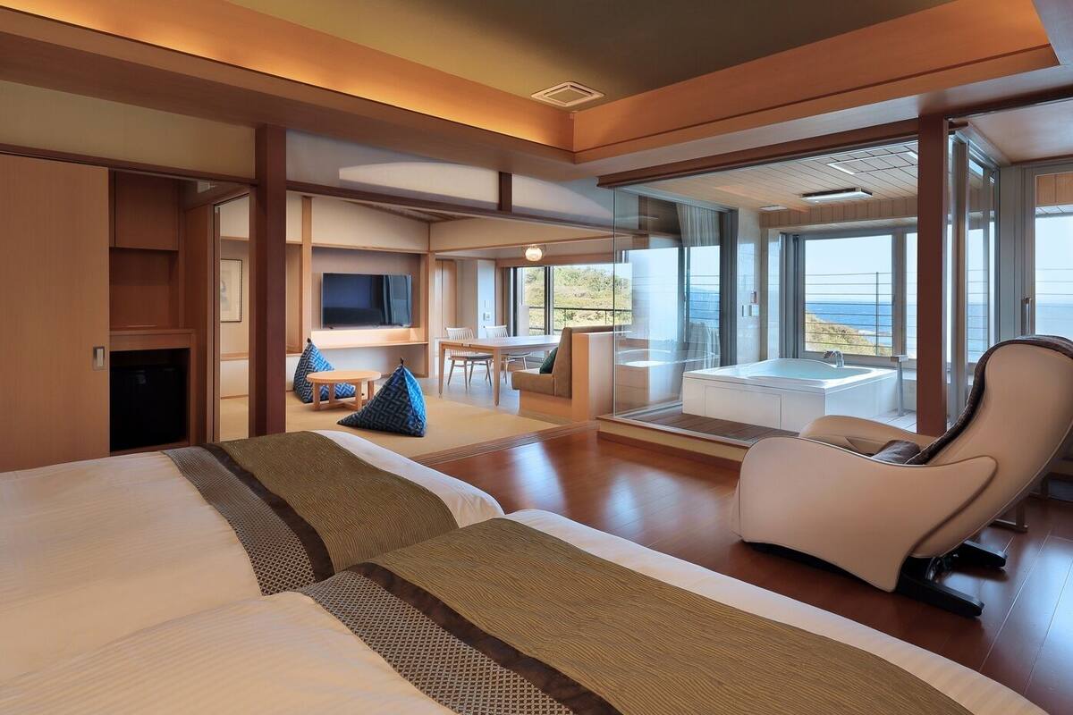 Una habitación de hotel moderna con una cama grande, zona de estar, televisión y balcón con vistas.