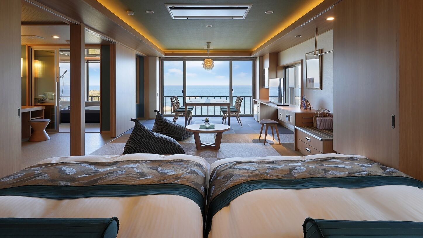 A room with two beds, a dining area, a small kitchen, and a balcony with a view.