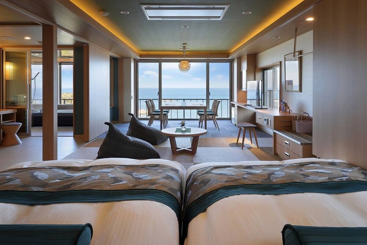 Una habitación con dos camas, zona de comedor, pequeña cocina y balcón con vistas.