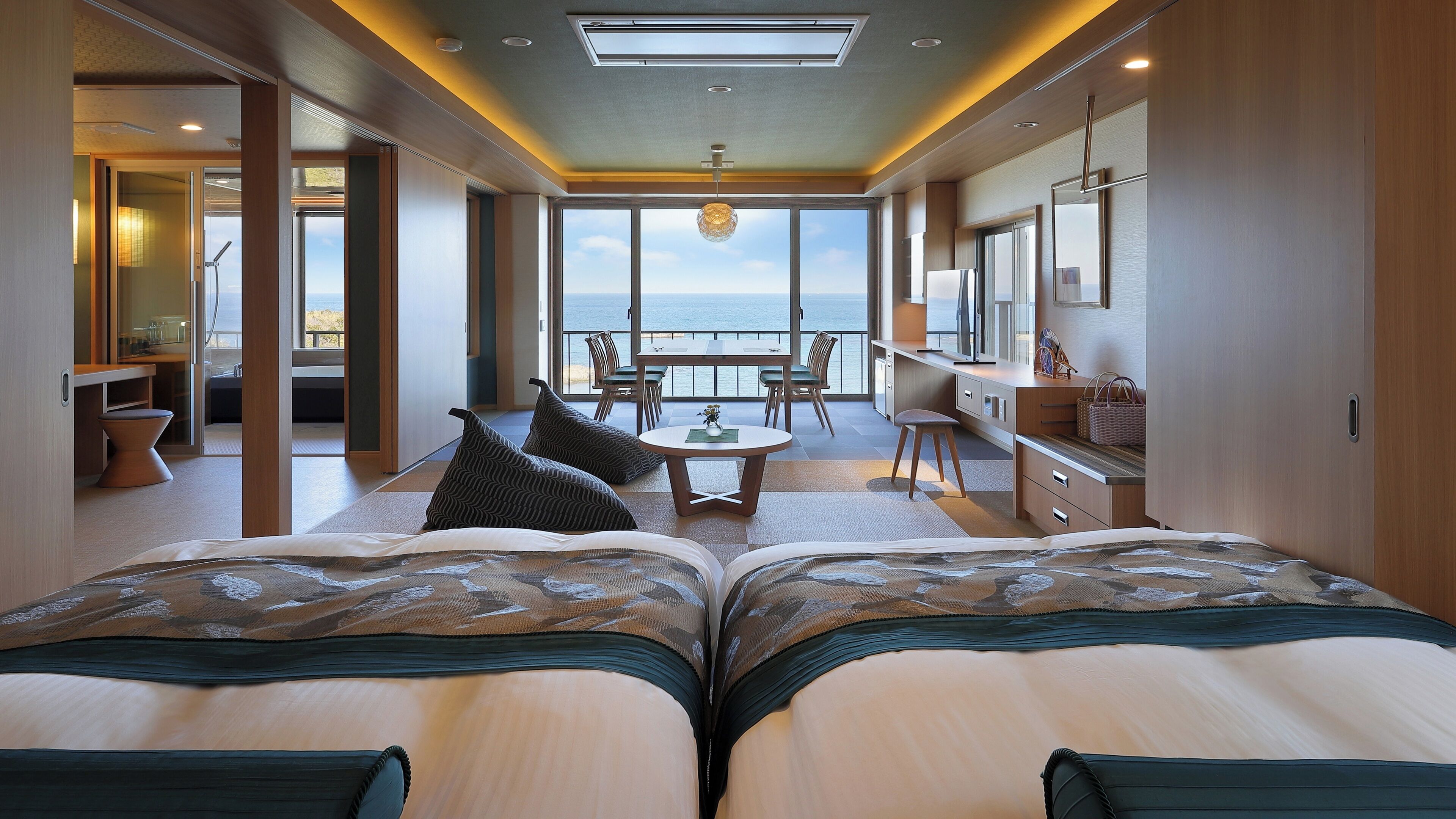 A modern hotel room with a large bed, a dining area, and a view of the sea.