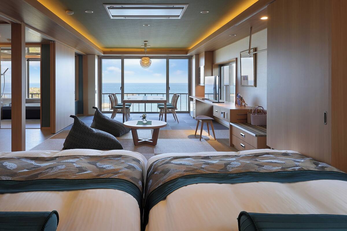 Una habitación de hotel moderna con una cama grande, un comedor y vista al mar.