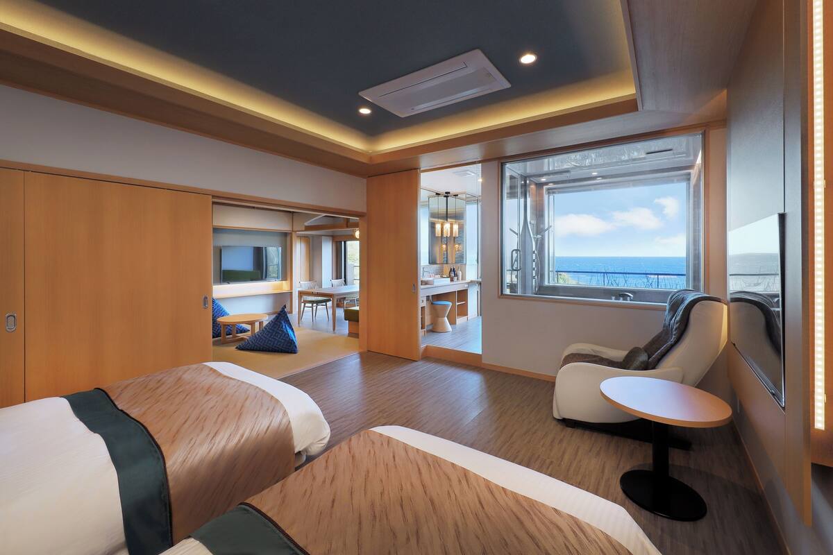 Una habitación de hotel moderna con dos camas, un área de comedor y vista al mar.