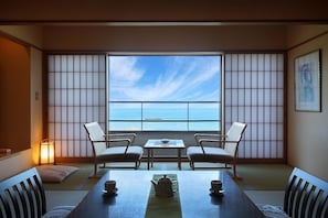 Una habitación con esteras de tatami, una mesa baja con dos sillas, vista al mar y un cuadro en la pared.