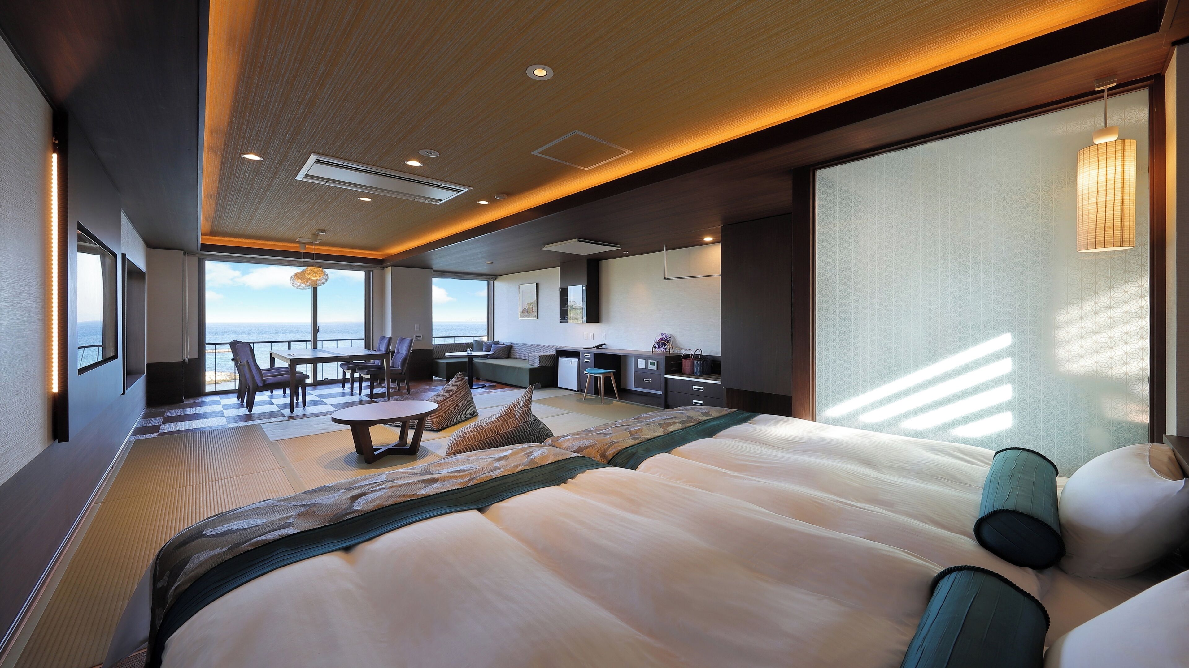 A modern hotel room with a large bed, a dining area, a kitchen, and a view of the ocean.
