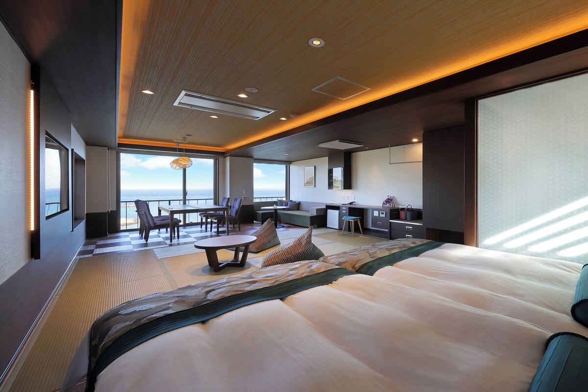 Una habitación de hotel moderna con una cama grande, un área de comedor, una cocina y vistas al océano.