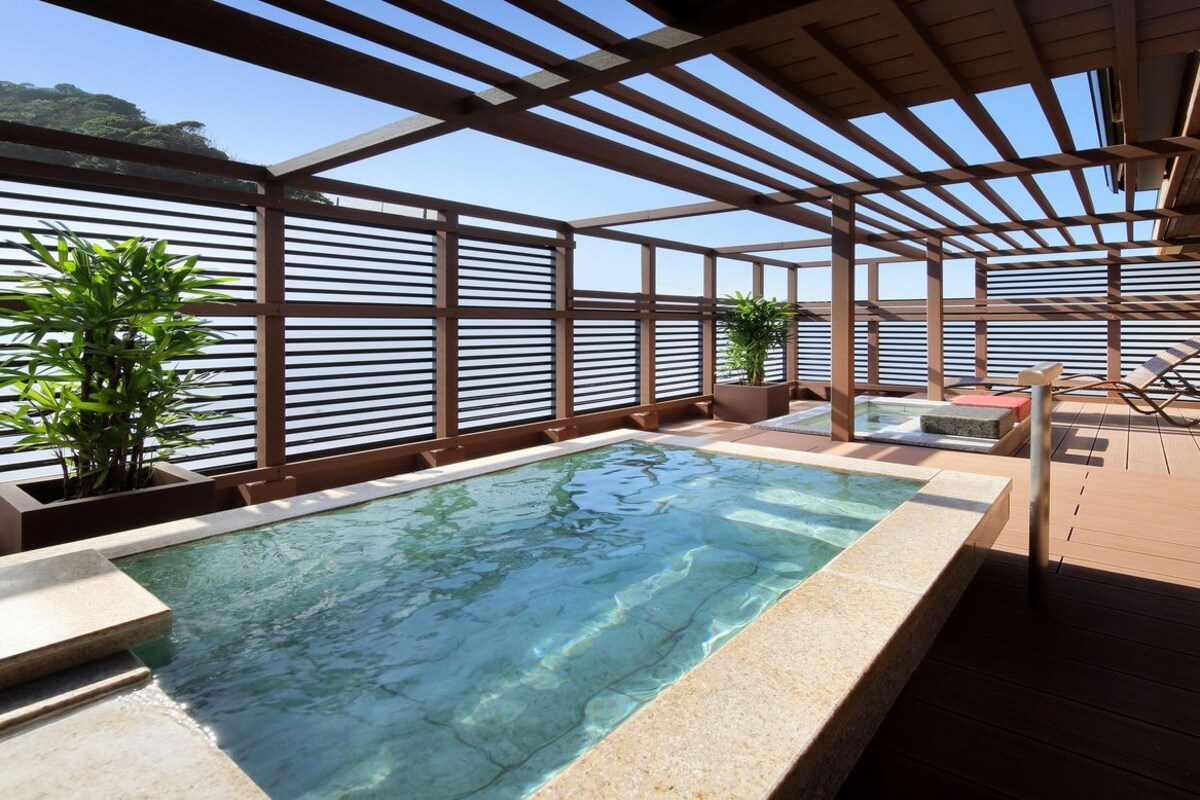Zona de piscina en la azotea con vistas despejadas al cielo, terraza de madera y sillones de descanso.