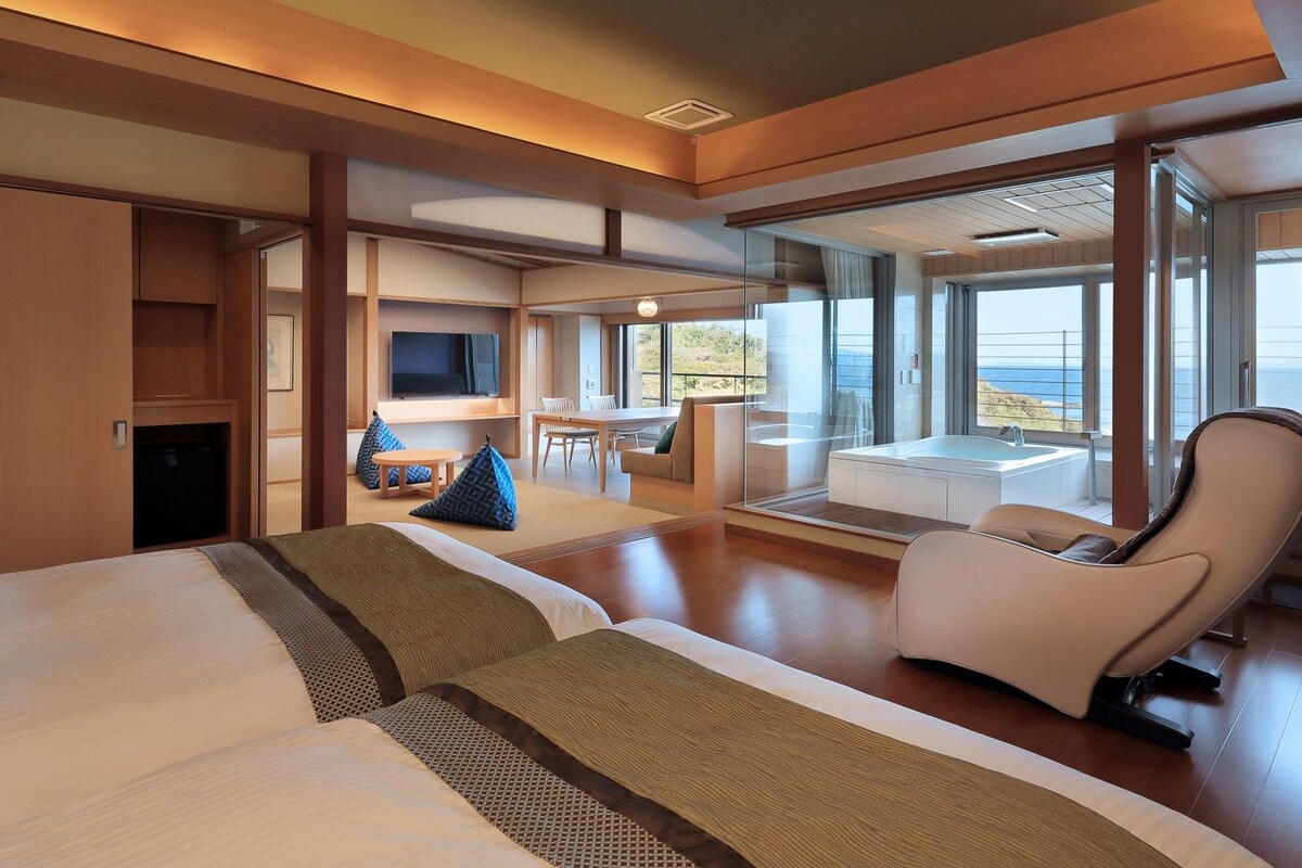 Una habitación de hotel moderna con una cama grande, zona de estar, televisión y balcón con vistas.