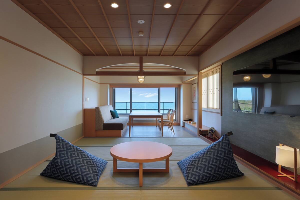 Una habitación japonesa tradicional con suelo de tatami, una mesa de madera baja, cojines y vista al mar.