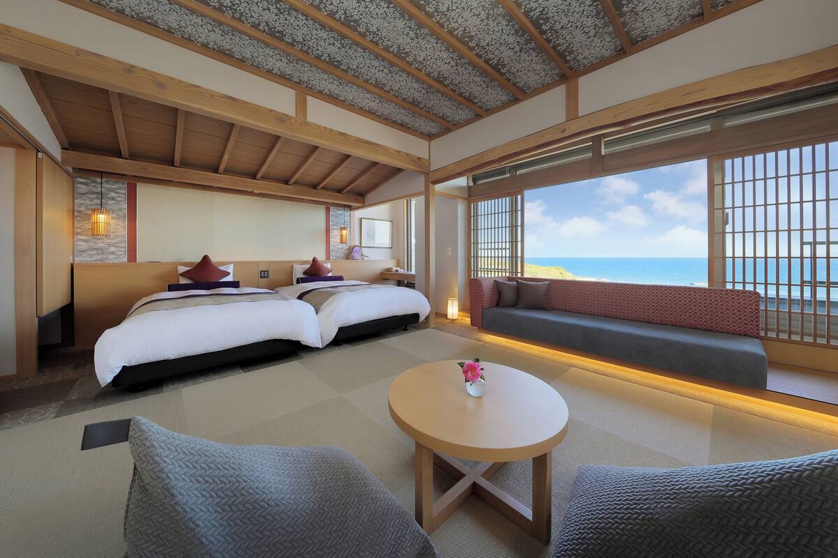 Habitación de hotel con una cama grande, un sofá, una mesita y vista al mar.