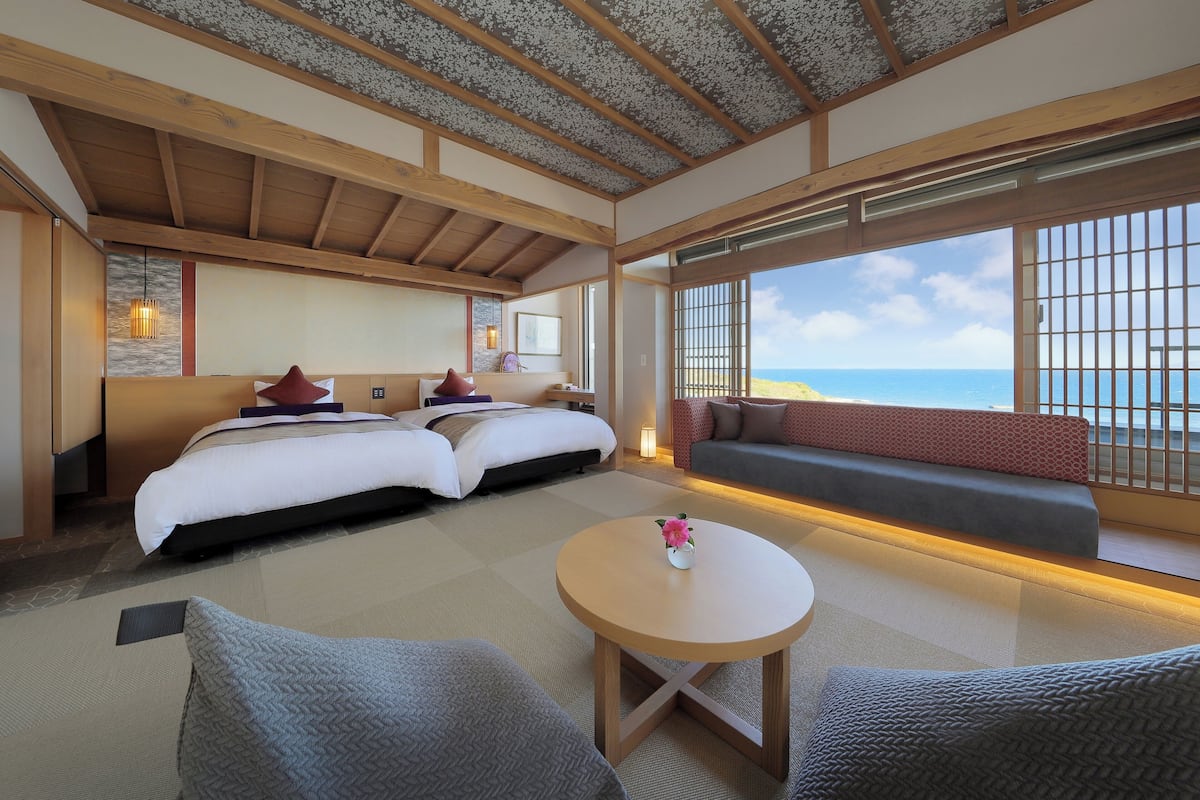 Habitación de hotel con una cama grande, un sofá, una mesita y vista al mar.