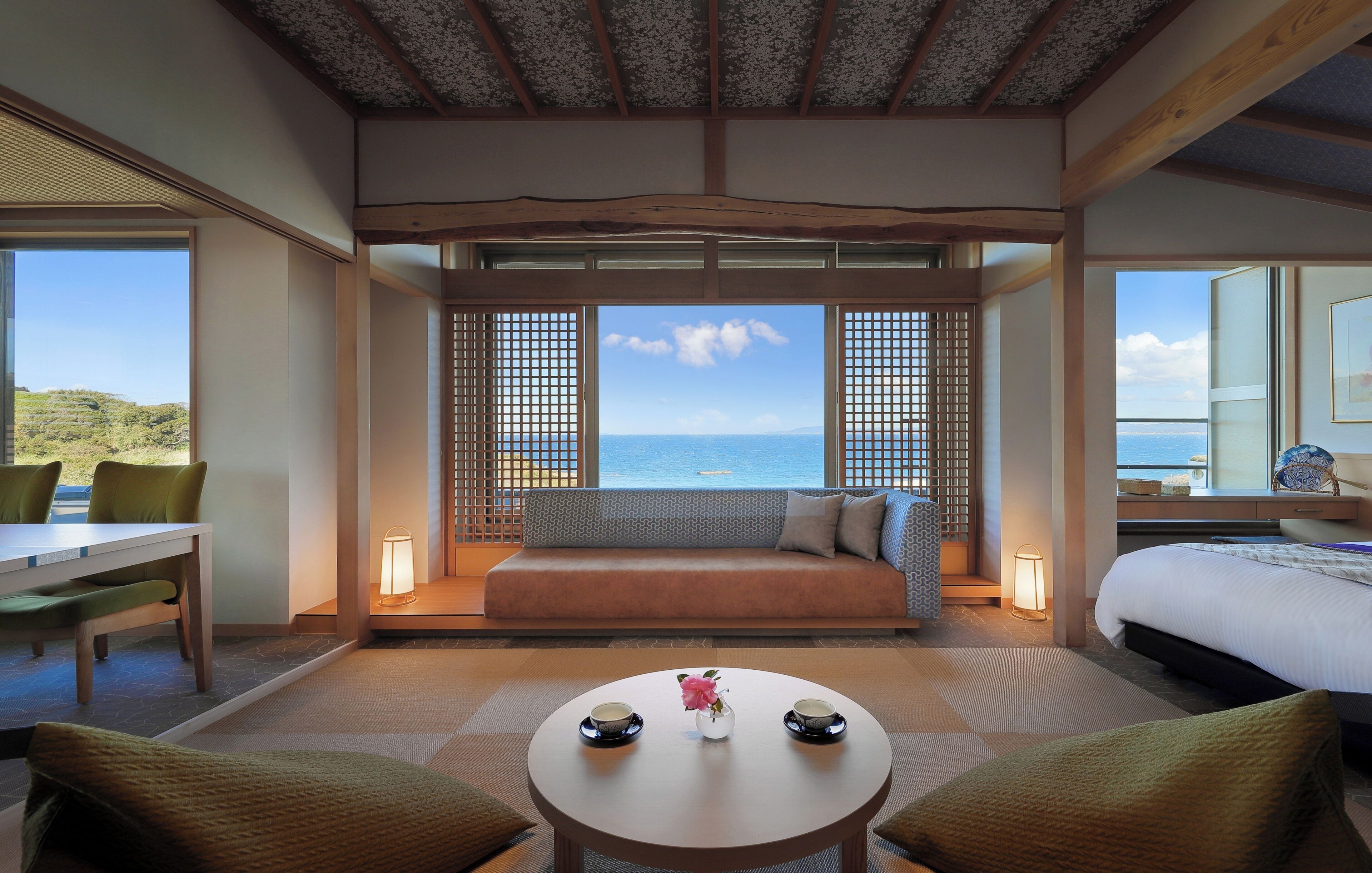 A room with a sofa, a dining table, and a view of the sea.