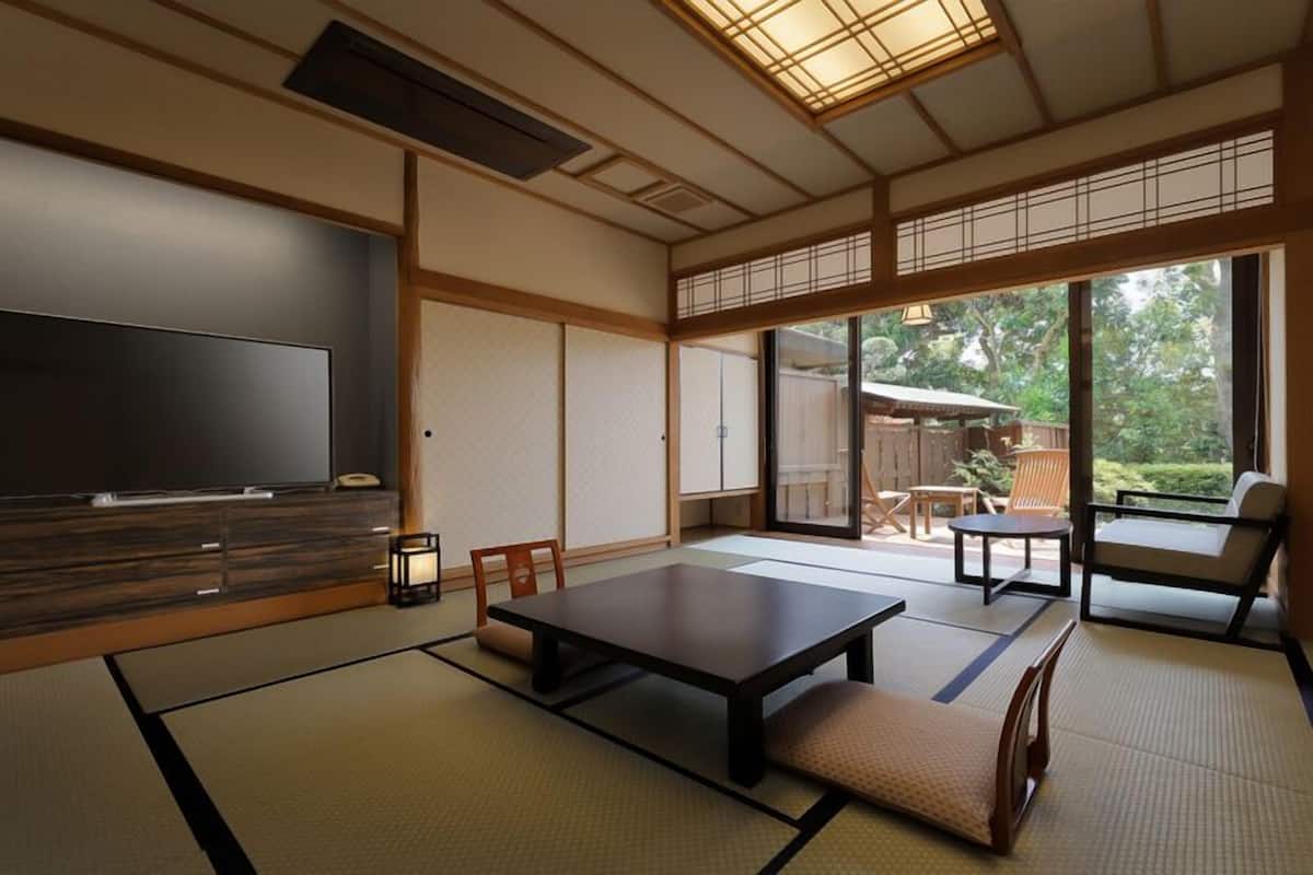 A traditional Japanese-style room with tatami flooring, a television, a low table, and a sliding door leading to an outdoor area.