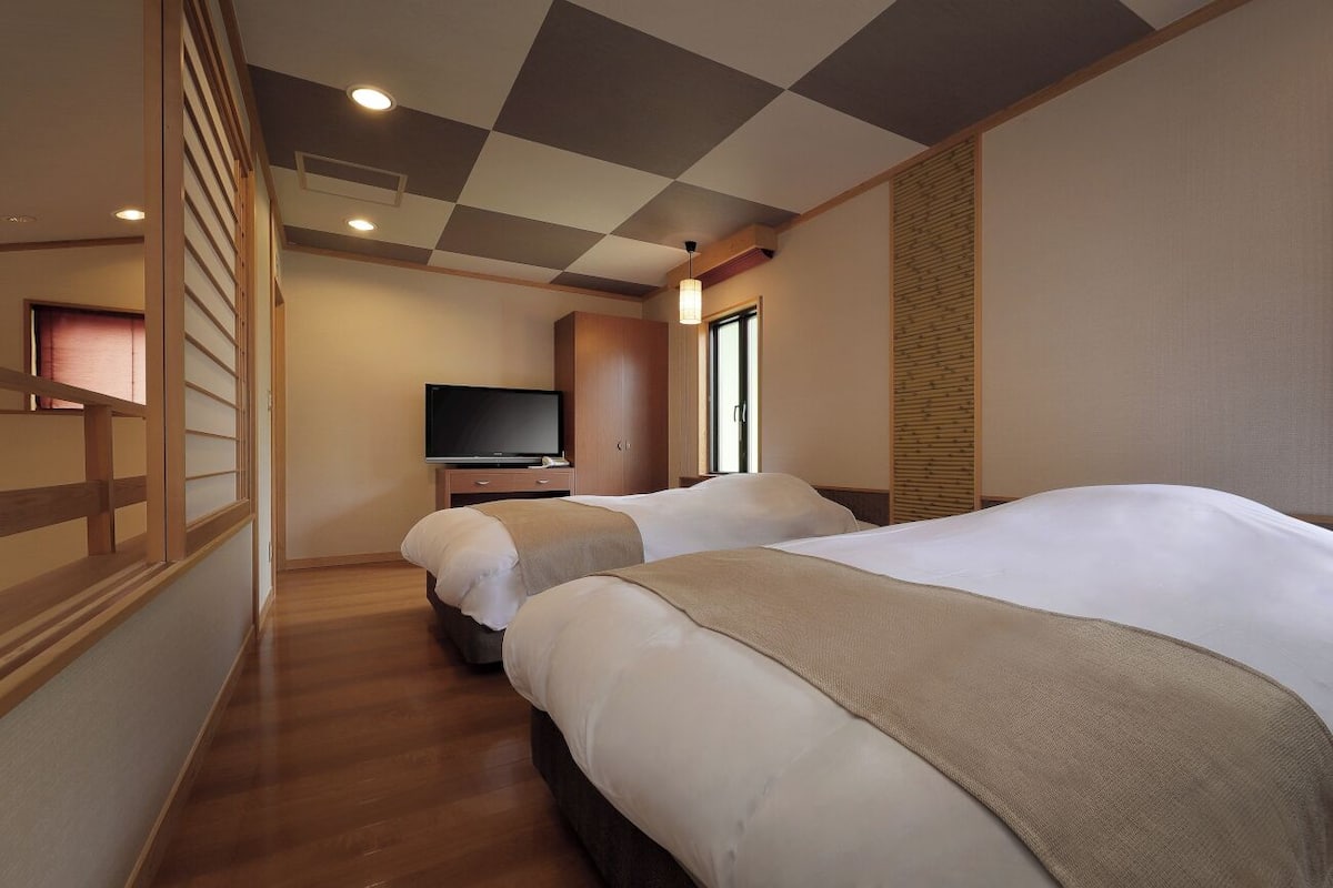 A hotel room with two beds, a television, and a window.