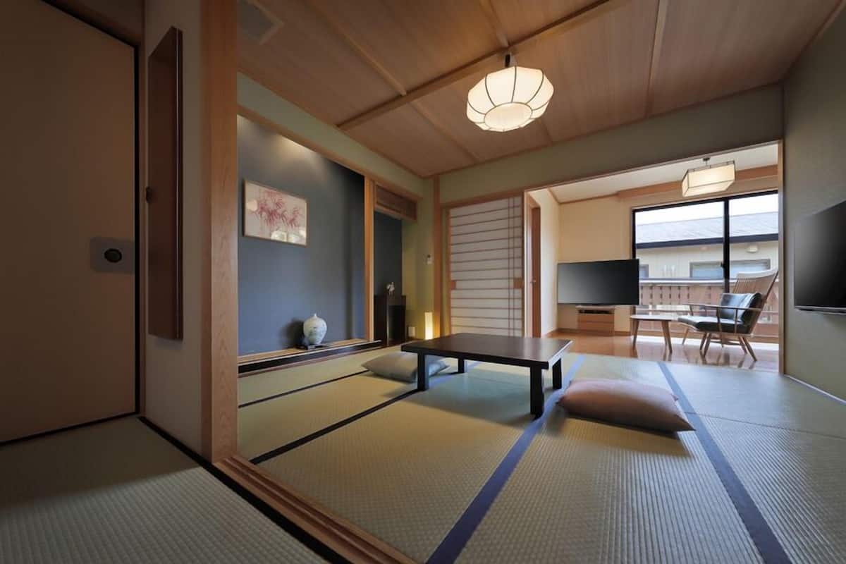 A traditional Japanese room with tatami flooring, a low table, a sofa, and a television.