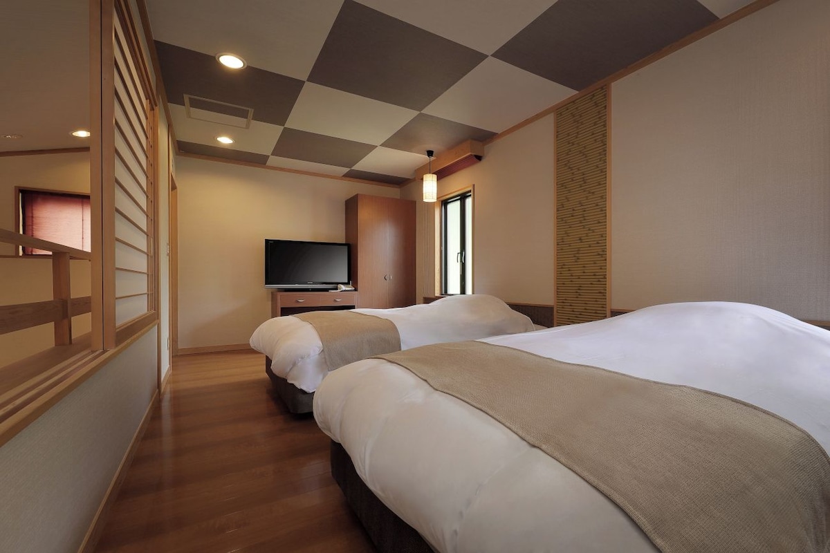 A hotel room with two beds, a television, and a window.