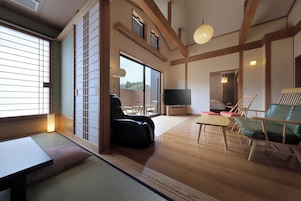 A traditional Japanese-style living room with tatami flooring, a low table, a sofa, and a television.