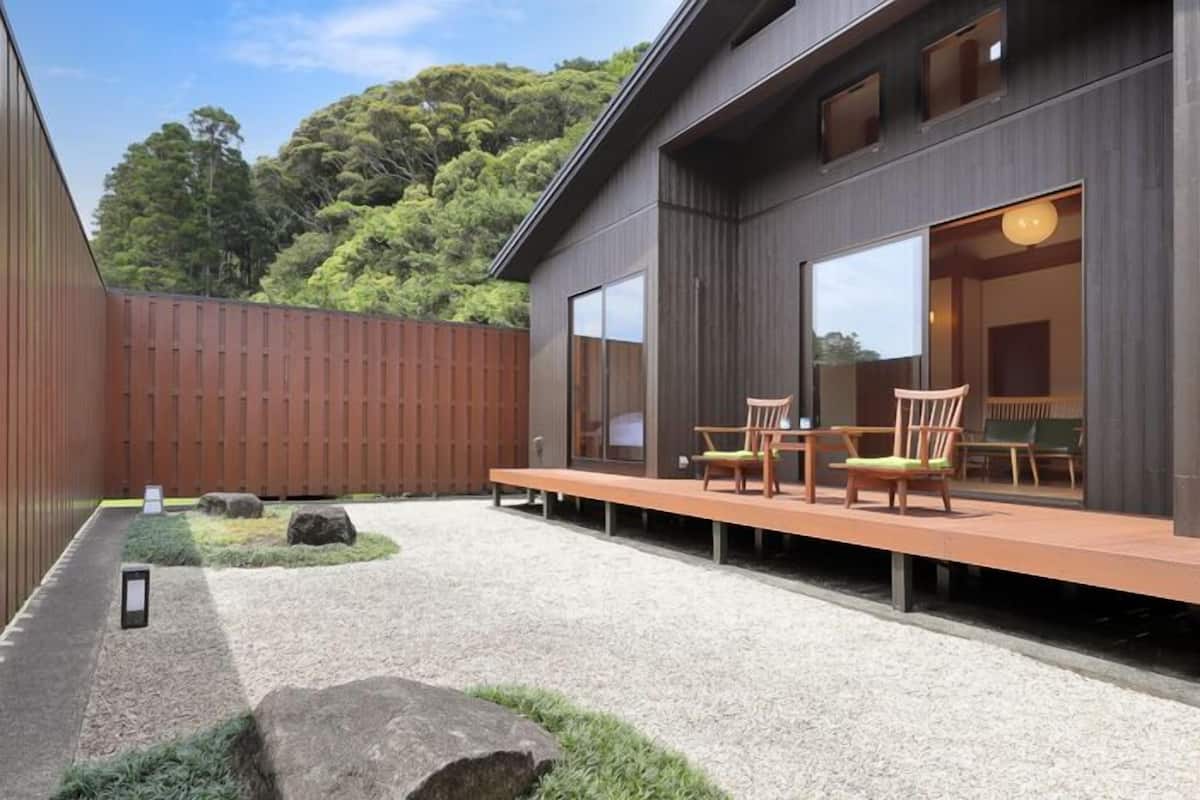 A modern building with a patio area featuring outdoor seating and a view of a forested area.