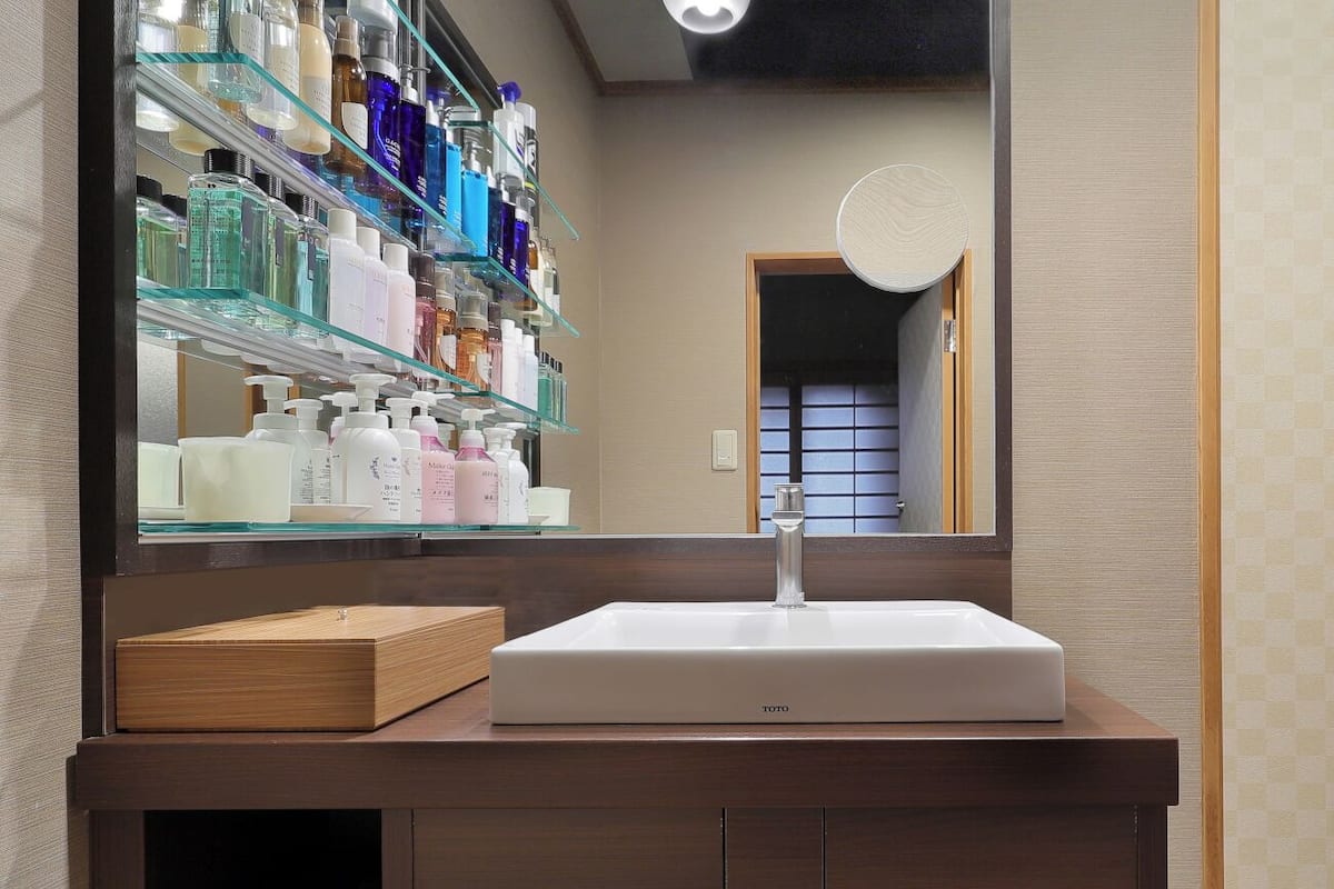 A bathroom with a white sink, a mirror, and shelves with various toiletries.