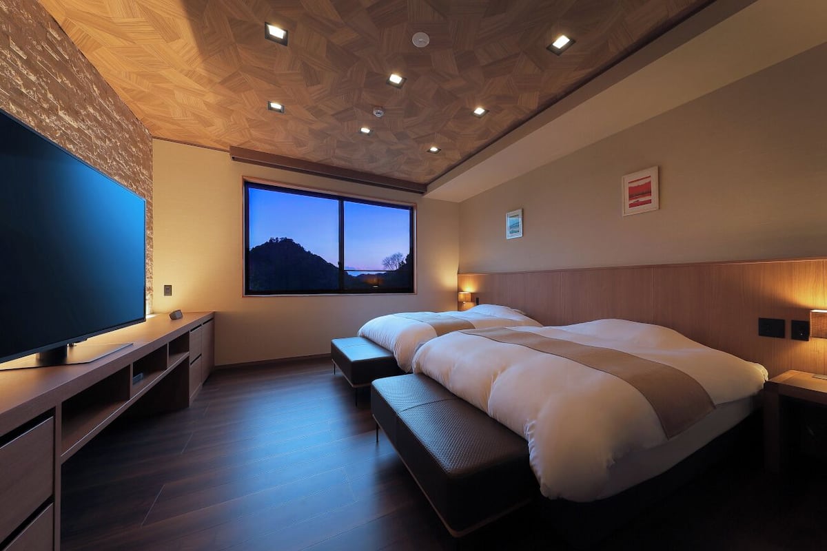 A modern bedroom with a large bed, a TV, and a window with a view of a mountain.