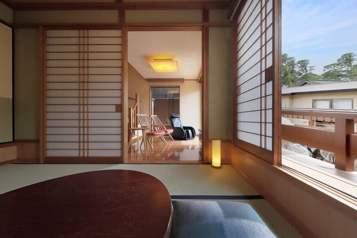 A traditional Japanese room with tatami flooring, a low table, sliding doors, and a view of the outside.