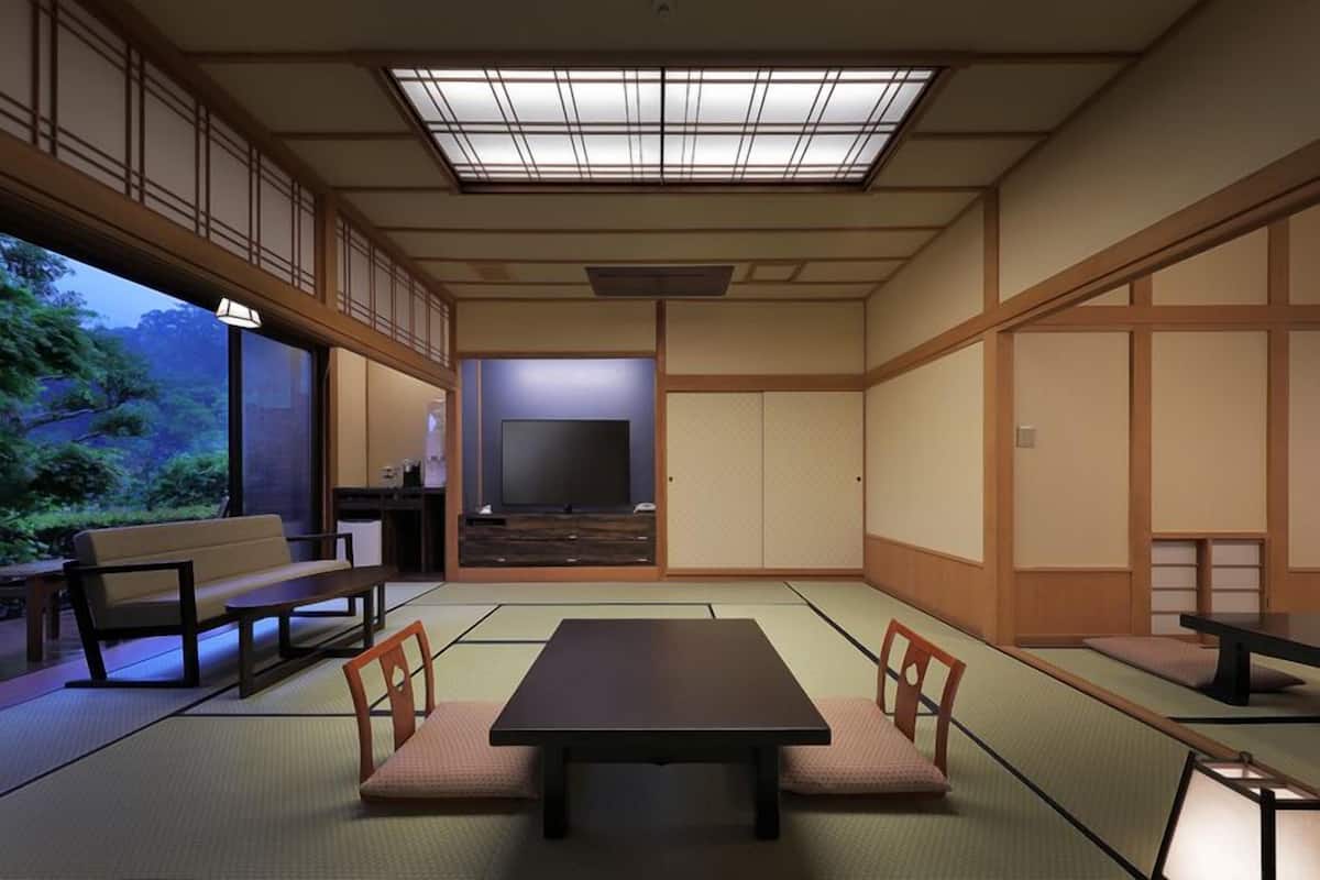 A traditional Japanese room with tatami flooring, a low table, chairs, a television, and sliding doors.