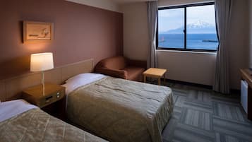 A hotel room with two beds, a desk, a chair, a lamp, a window with a view of mountains and the sea, and a painting on the wall.