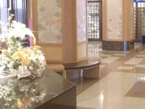 Un área de recepción con mostrador de atención al cliente, un jarrón de flores y un mostrador de registro.