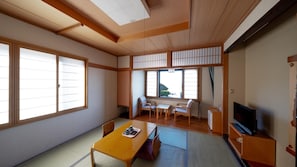 Una habitación tradicional japonesa con suelo de tatami, una mesa de madera baja, un televisor y puertas correderas shoji.