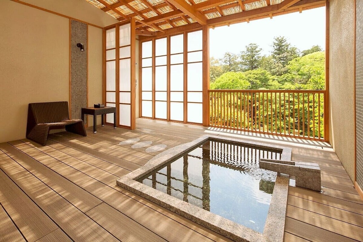A traditional Japanese-style room with tatami flooring, a small water feature, and a balcony with a view of greenery.