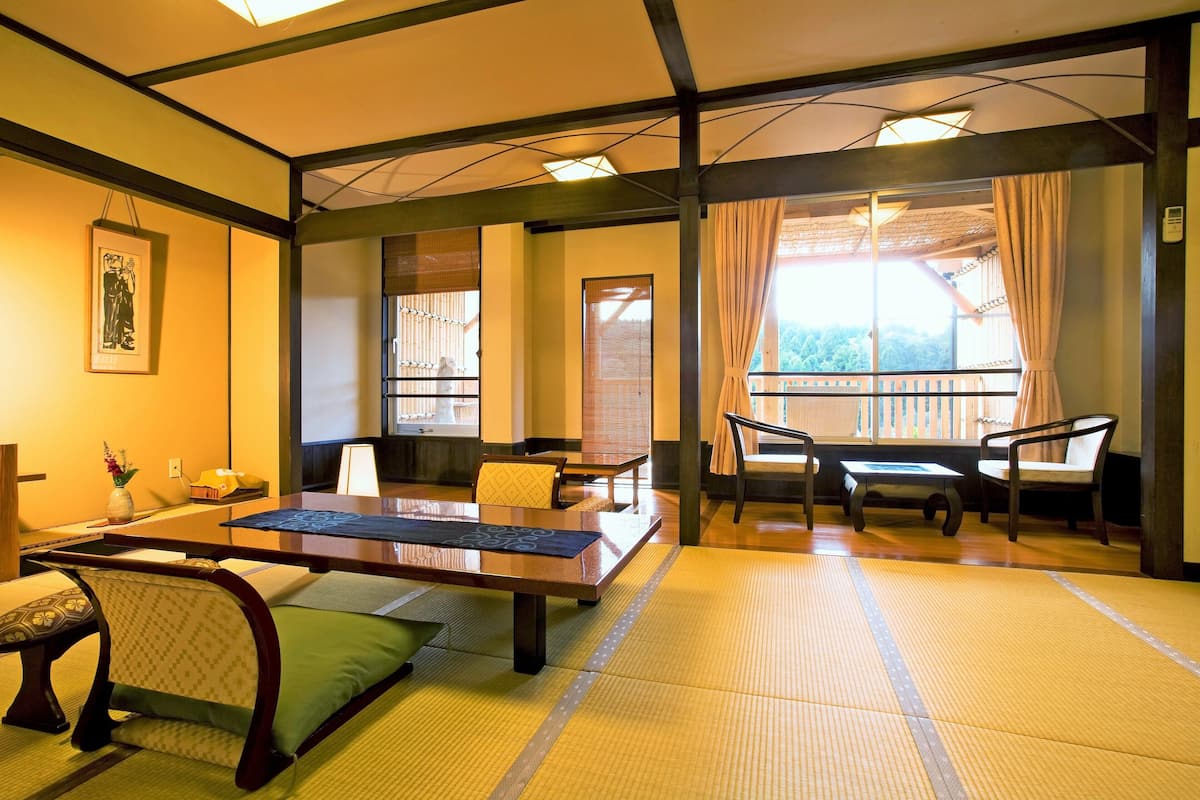 A traditional Japanese room with tatami flooring, a low table, chairs, and a view of the outdoors.
