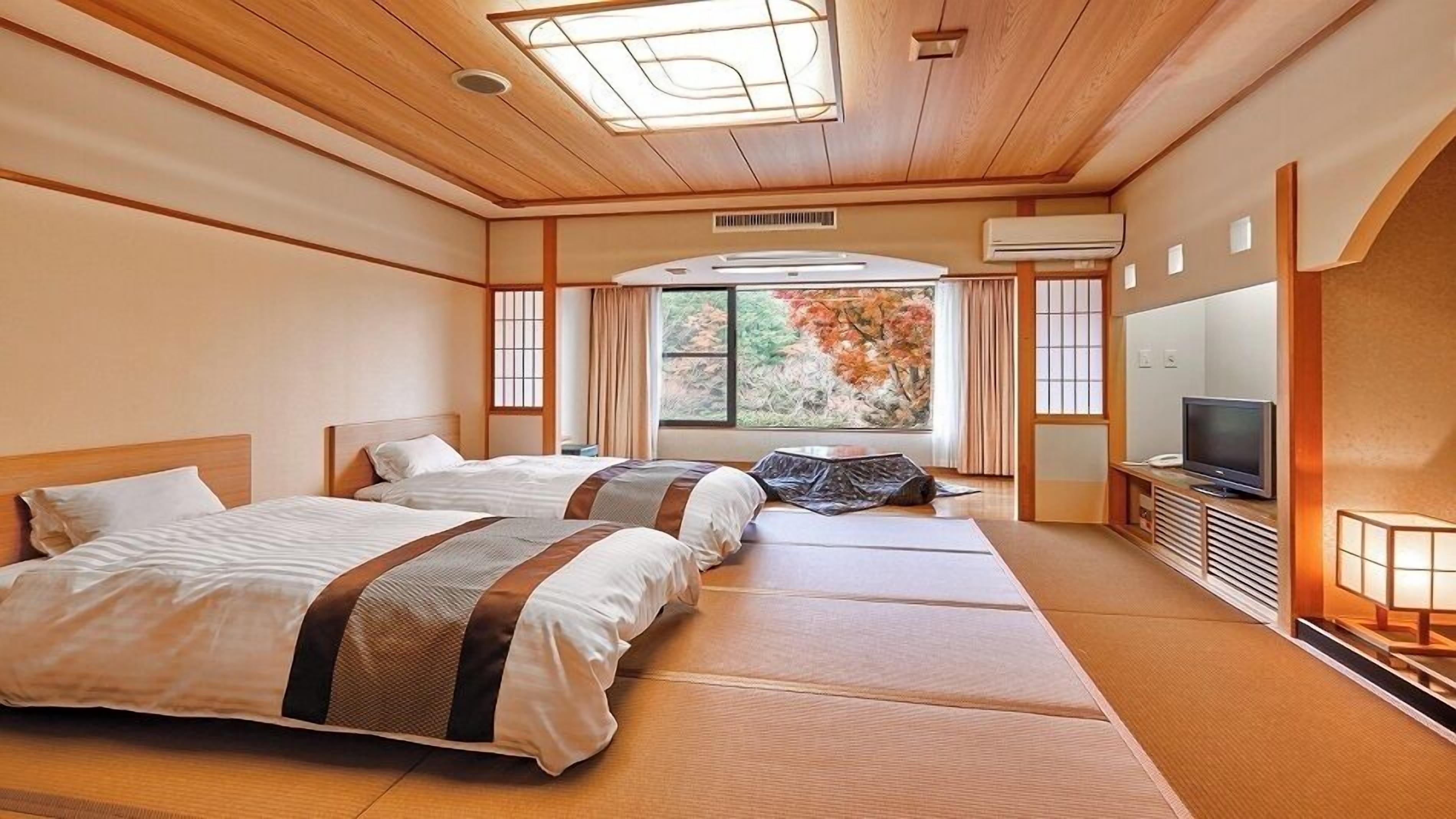 A hotel room with two beds, a TV, an air conditioning unit, and a large window with a view of trees.