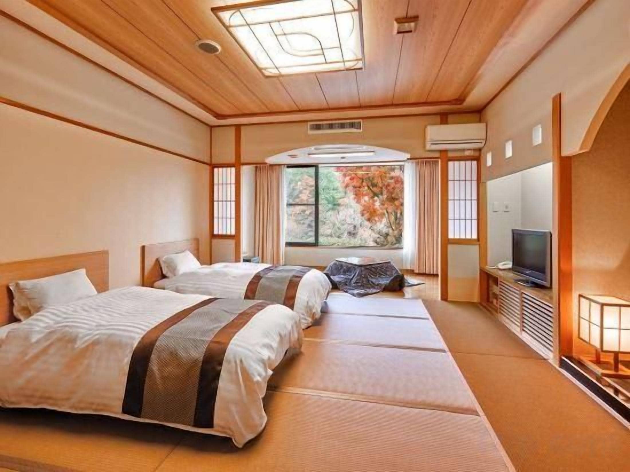 A traditional Japanese-style room with tatami flooring, two beds, a television, and a view of autumn foliage.