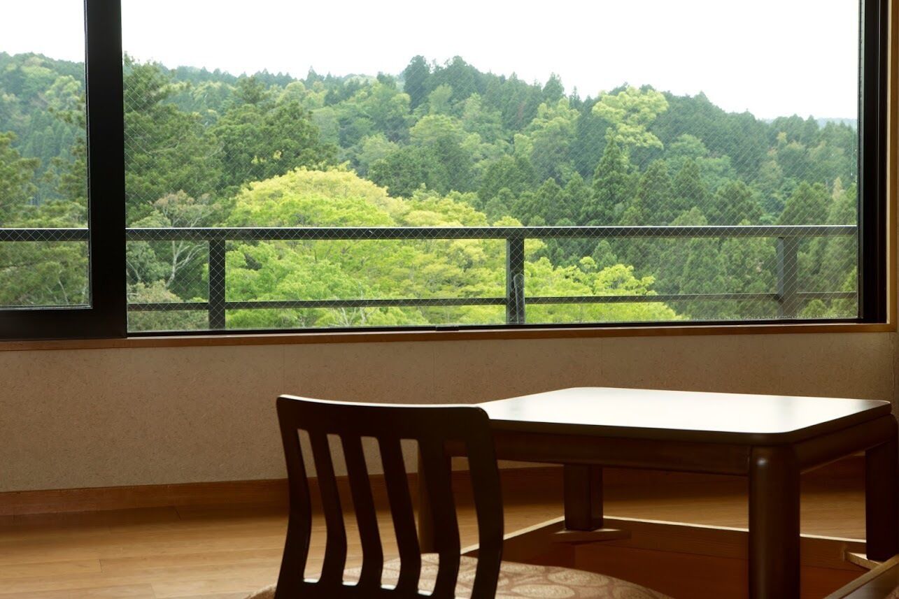 A room with a large window, a wooden chair, and a table.