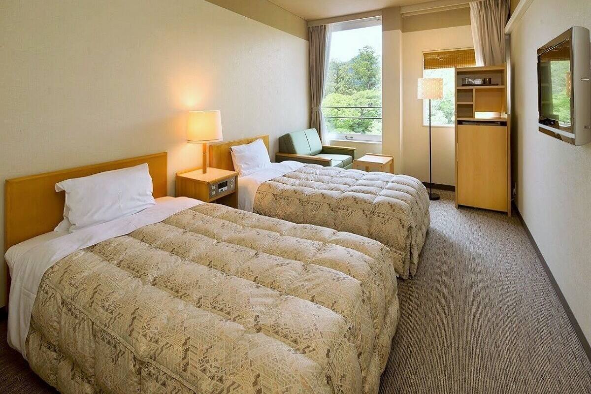 A hotel room with two beds, a TV, a desk, a lamp, and a window with a view.