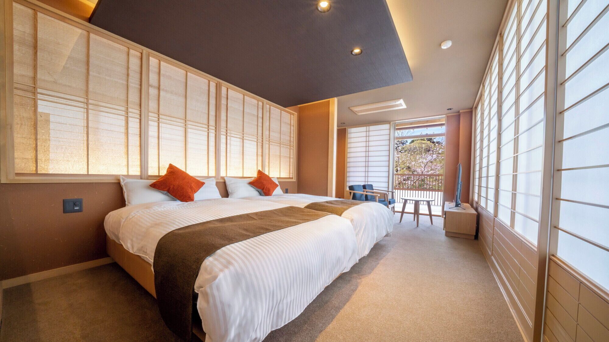 A bedroom with a large bed, a view of the outdoors, and a balcony with seating.