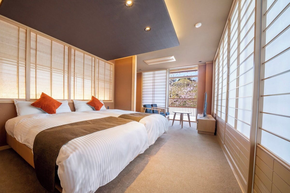 A bedroom with a large bed, a view of the outdoors, and a balcony with seating.