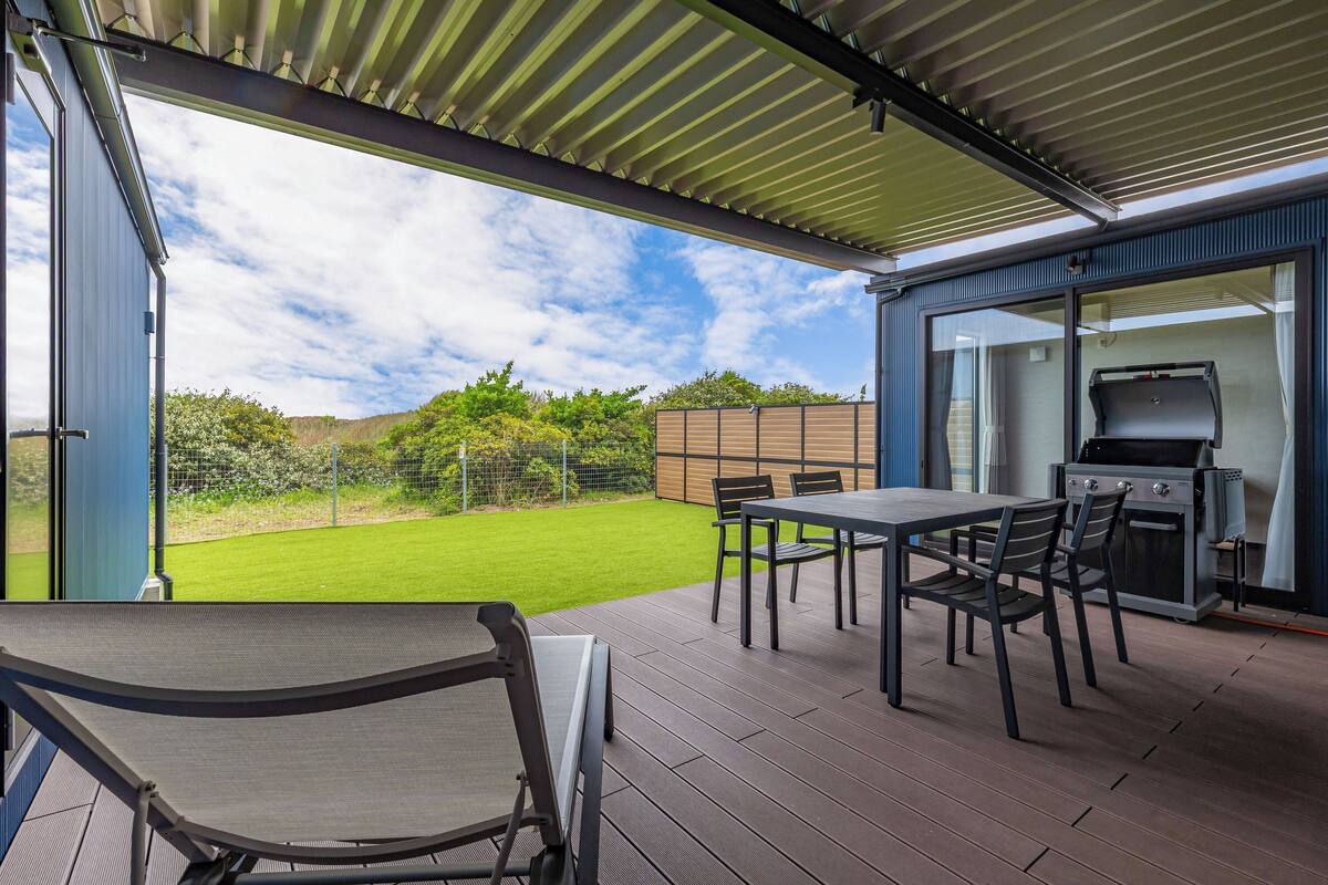 An outdoor patio with a table and chairs, a grill, and a view of a green lawn and trees.
