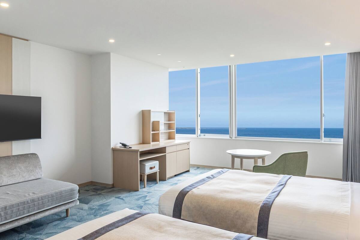 A hotel room with a bed, a desk, a chair, a TV, and a view of the ocean.